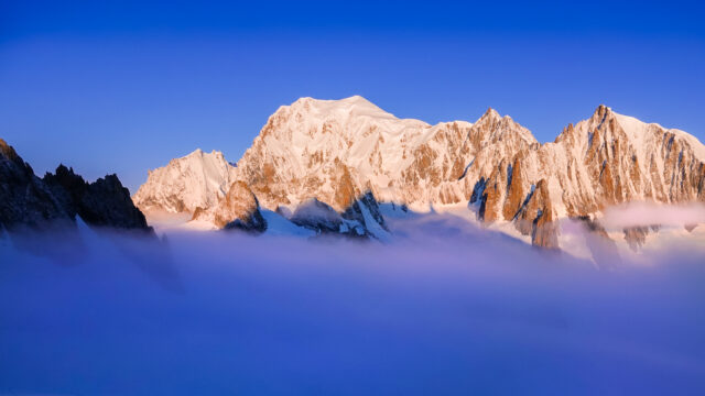 Life Happens Outdoors view of Mont Blanc above the clouds at sunrise with alpenglow, seen from the Vallée Blanche in the French Alps.