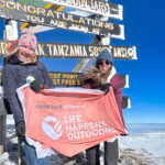 Two Life Happens Outdoors community members on Uhuru Peak holding the Life Happens Outdoors flag