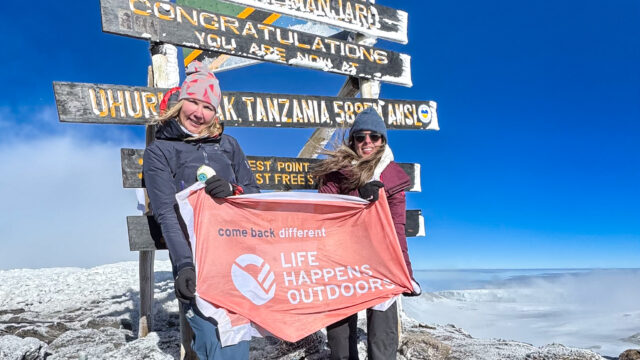 Two Life Happens Outdoors community members on Uhuru Peak holding the Life Happens Outdoors flag