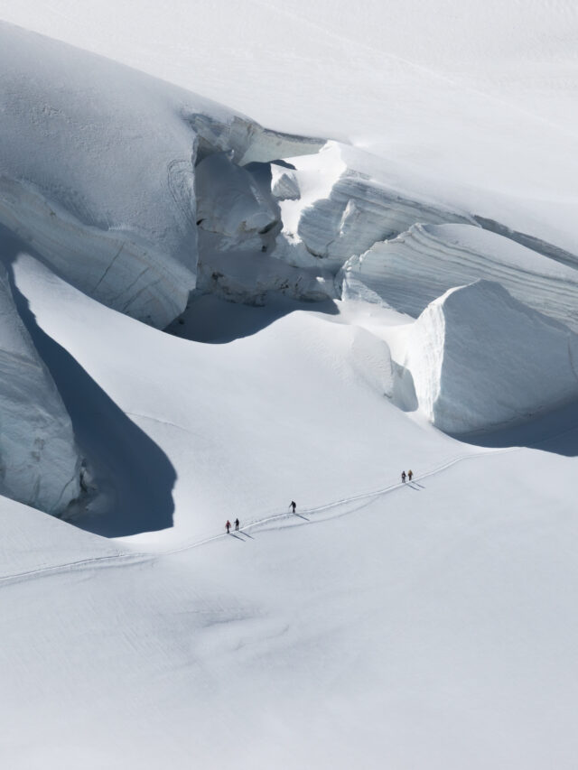 Roped climbers crossing a glacier beneath towering seracs during a mountaineering trip in the Alps