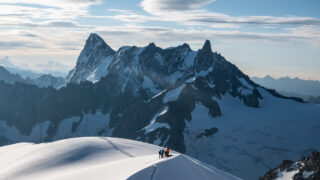 Mountaineers standing on a snowy ridge with dramatic alpine peaks in the background