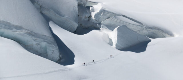 Guided climbers traversing a glacier below large ice formations in the Alps