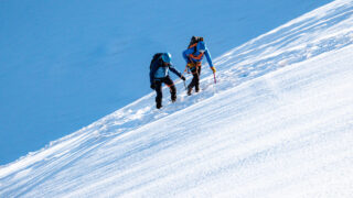 Two climbers ascending a steep snow slope during a guided mountaineering trip in the Alps