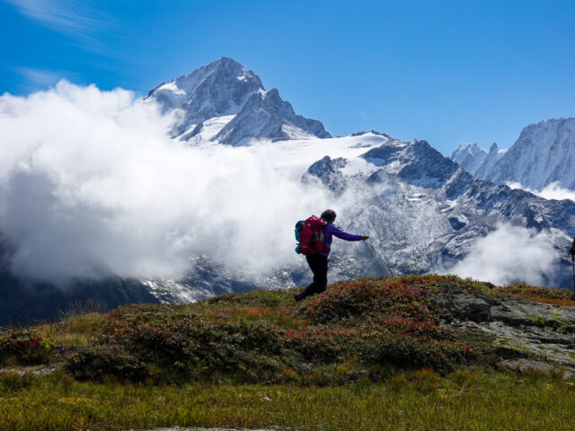 Hiker crossing alpine terrain beneath clouds and snowy peaks during a hiking trip in the Alps
