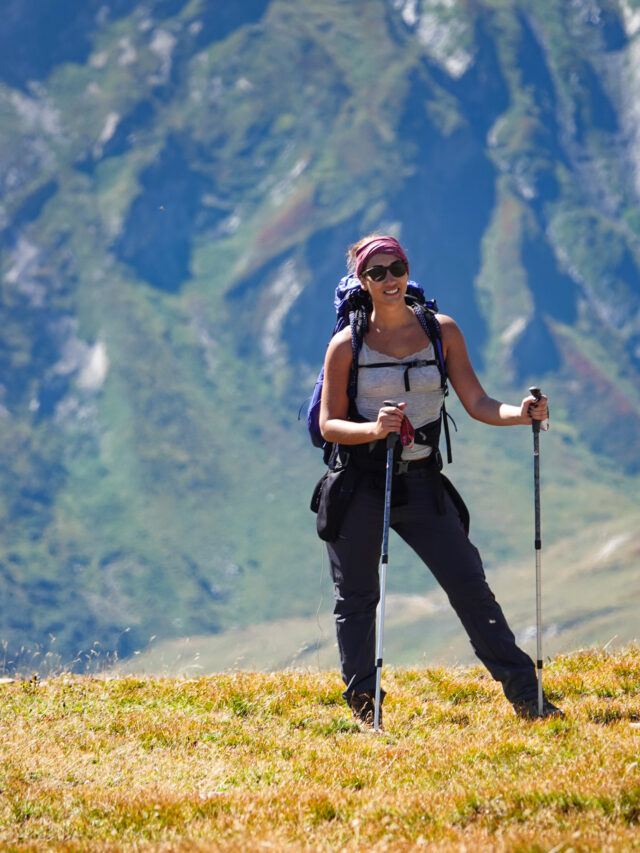 Woman hiker crossing an alpine meadow with trekking poles during a hiking trip in the Alps