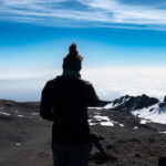 Climber looking out over the summit landscape of Kilimanjaro above a blanket of clouds