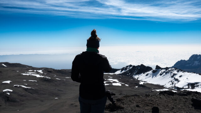 Climber looking out over the summit landscape of Kilimanjaro above a blanket of clouds