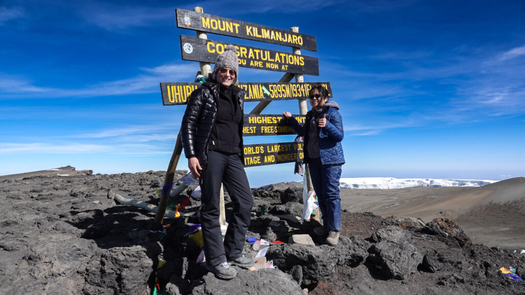 Two climbers posing at the Uhuru Peak summit sign on Mount Kilimanjaro