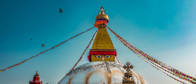 Boudhanath Stupa in Kathmandu Nepal with prayer flags and birds in the sky