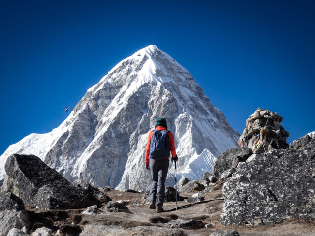 Trekker on a rocky mountain trail in Nepal facing a dramatic snow covered Himalayan peak