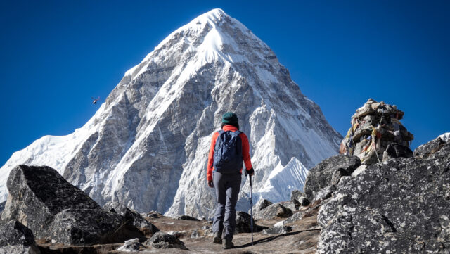 Trekker on a rocky mountain trail in Nepal facing a dramatic snow covered Himalayan peak