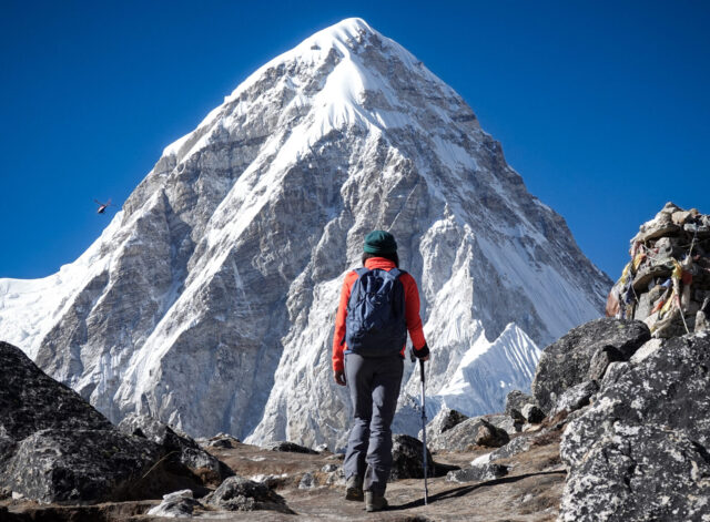 Trekker on a rocky mountain trail in Nepal facing a dramatic snow covered Himalayan peak