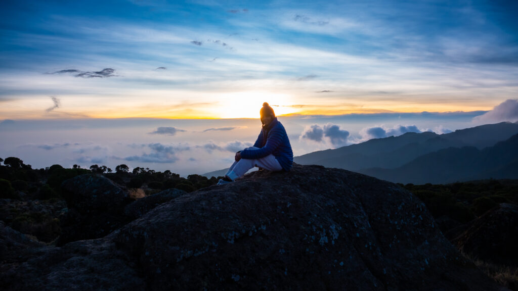 Life Happens Outdoors community member sitting on a rock at sunrise on Kilimanjaro, reflecting on overcoming fear through adventure
