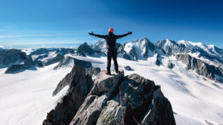 Mountaineer standing on a rocky summit above glaciers and snowy peaks in the Alps
