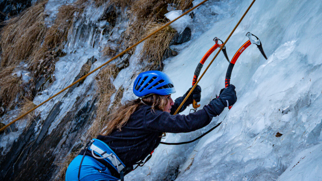 Ice climber ascending frozen rock during a guided outdoor challenge