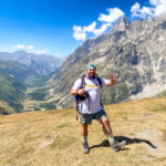 Trekker celebrating on the Grand Col Ferret approach with the Italian Val Ferret and Mont Blanc massif in the background