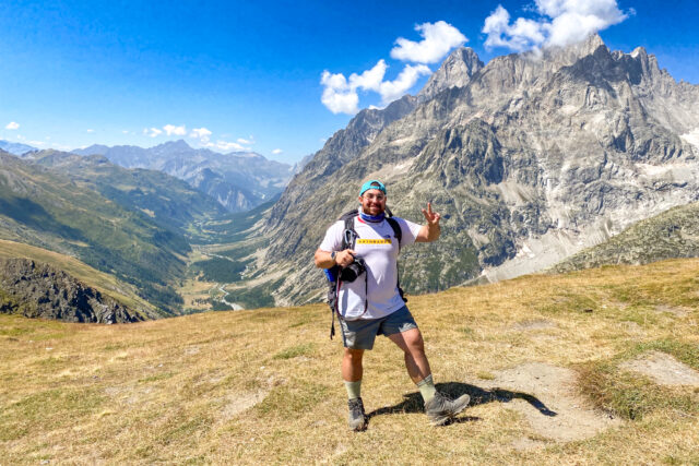 Trekker celebrating on the Grand Col Ferret approach with the Italian Val Ferret and Mont Blanc massif in the background