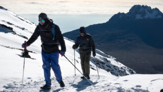 Two trekkers ascending snowy slopes on Kilimanjaro with Mawenzi in the background.