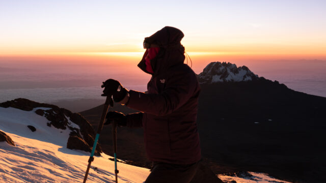 Climber pausing on Kilimanjaro at sunrise with Mawenzi silhouetted behind.