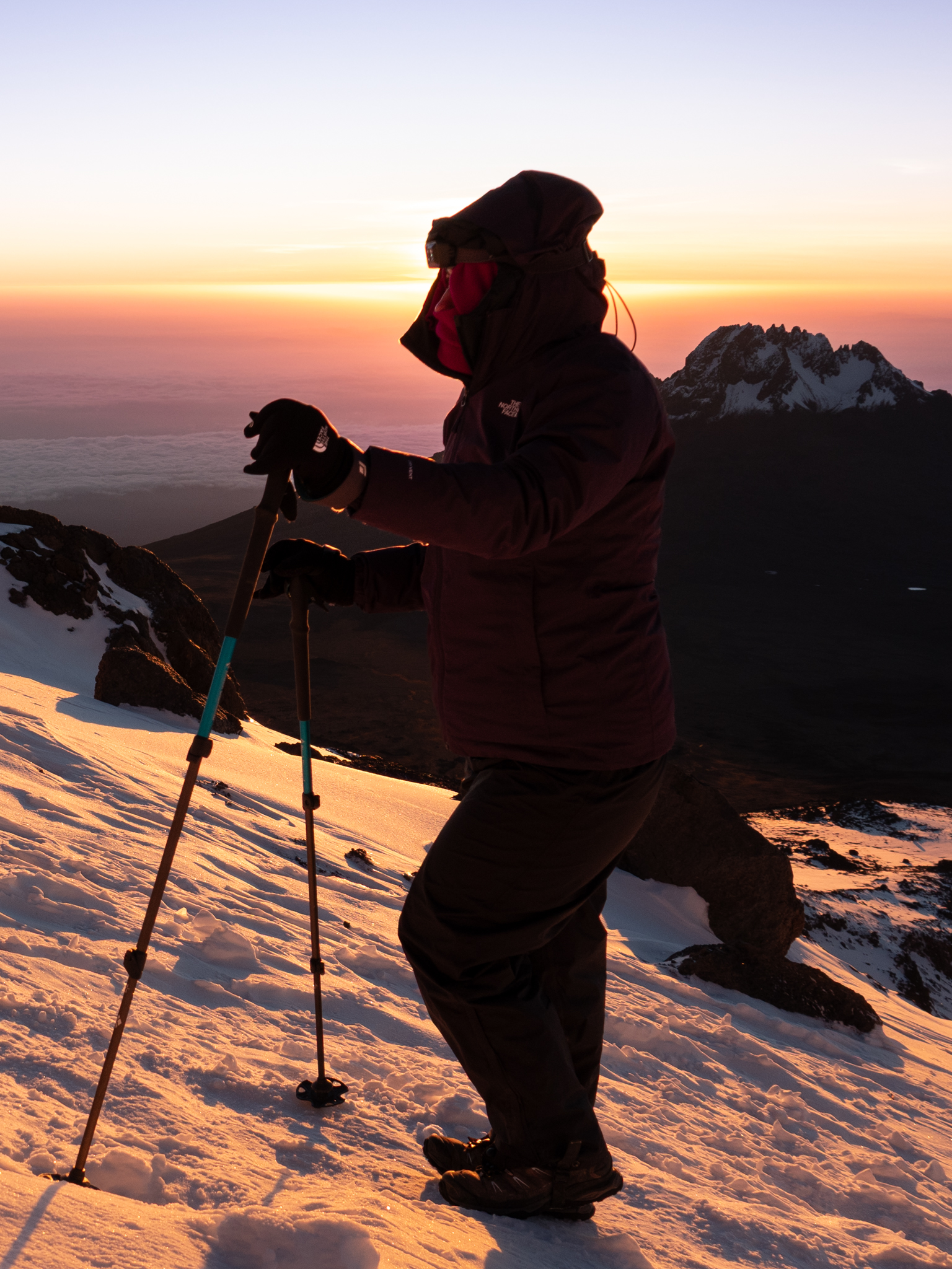 Hiker on the snowy slopes of Kilimanjaro at sunrise with Mawenzi in the background.