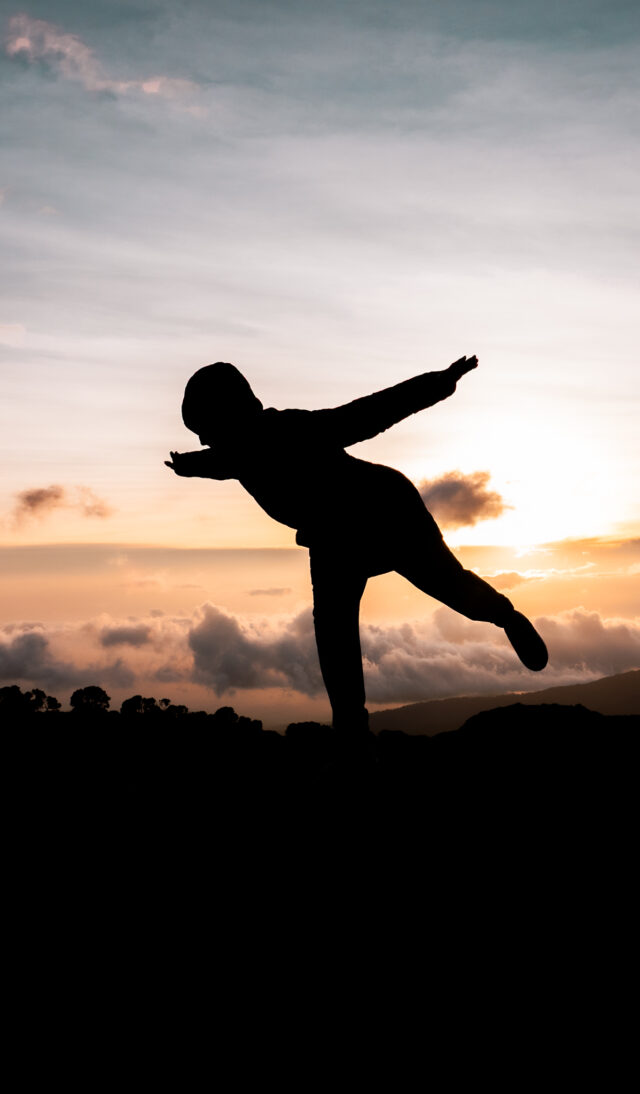 Silhouette of a person at sunset on Kilimanjaro with clouds and mountain ridges in the background.