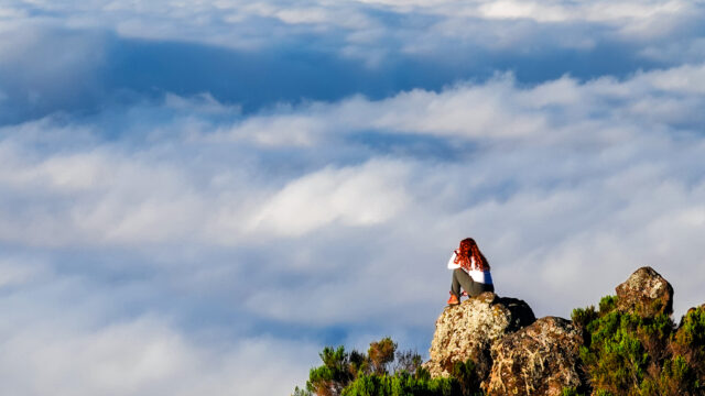 Hiker sitting on a rocky viewpoint above the clouds on Mount Kilimanjaro.