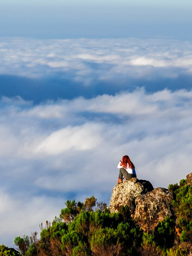 Hiker on a rocky viewpoint above the clouds during a Kilimanjaro trek.