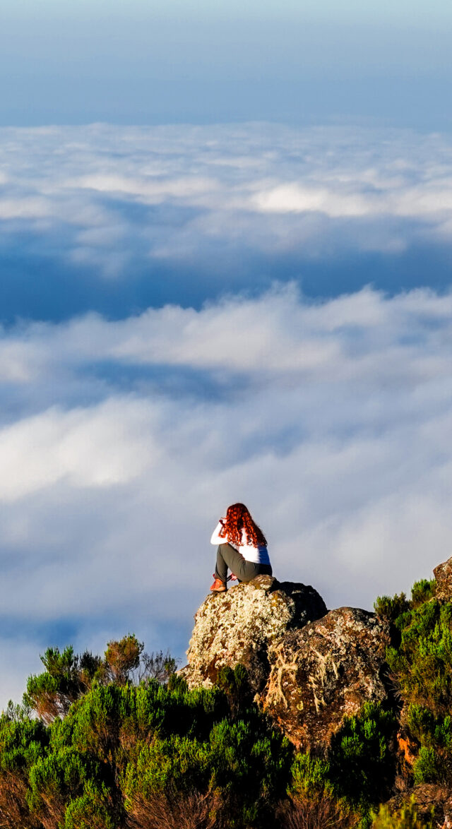 Hiker on a rocky viewpoint above the clouds during a Kilimanjaro trek.