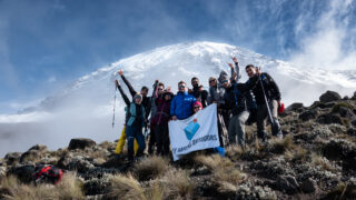 Life Happens Outdoors group posing below Mount Kilimanjaro with snow covered slopes behind.