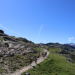 Hikers walking on a high mountain section of the Tour du Mont Blanc route under clear blue skies