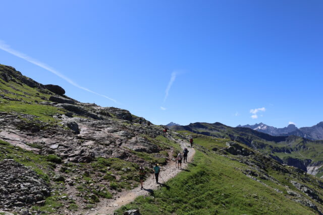 Hikers walking on a high mountain section of the Tour du Mont Blanc route under clear blue skies