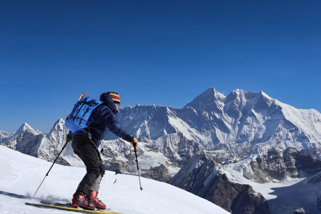 Skier descending Mera Peak glacier with Everest region mountains in the background during ski touring expedition