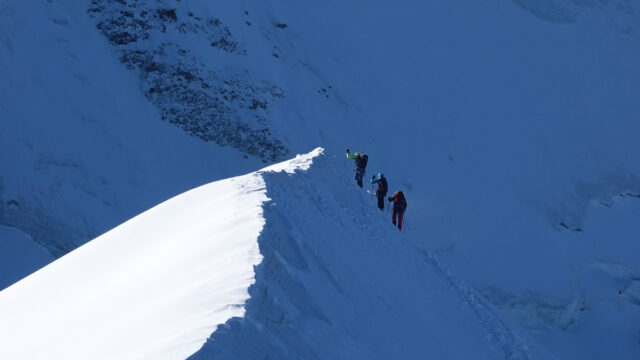 Climbers ascending a sharp corniced snow ridge during a guided Mont Blanc climb.