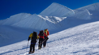 Team moving across a snowy glacier approach beneath the ice formations of Mont Blanc.