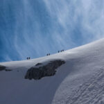 Guided team climbing a high snow ridge on Mont Blanc under a blue alpine sky