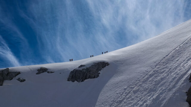 Guided team climbing a high snow ridge on Mont Blanc under a blue alpine sky