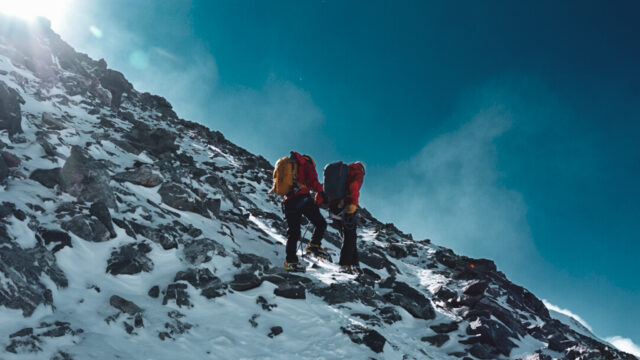 Two climbers ascending a rocky, snow covered upper slope during a Mont Blanc summit approach.