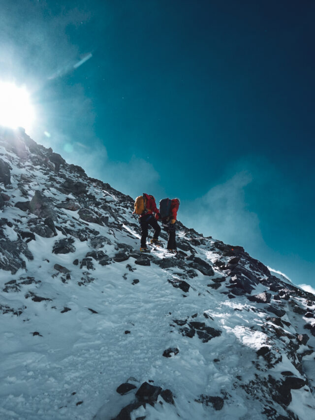 Two climbers moving uphill on a steep rocky and snowy slope high on Mont Blanc.