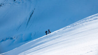 Two climbers ascending a steep snow slope below glacial ice while climbing Mont Blanc.