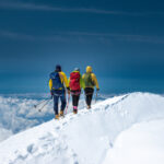 Three climbers walking the Mont Blanc summit ridge above a sea of clouds.