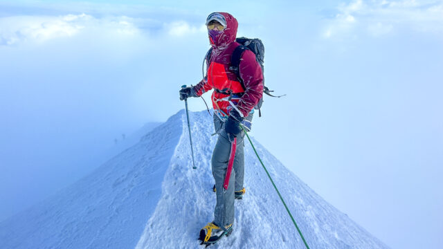 Climber standing on the narrow summit ridge of Mont Blanc above the clouds.