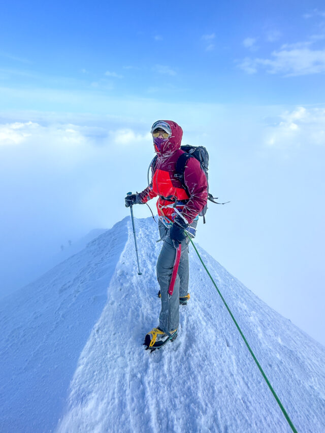 Climber on the exposed snowy summit ridge of Mont Blanc in high alpine cloud.