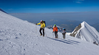 Three climbers traversing the upper snow slopes during a guided climb on Mont Blanc.