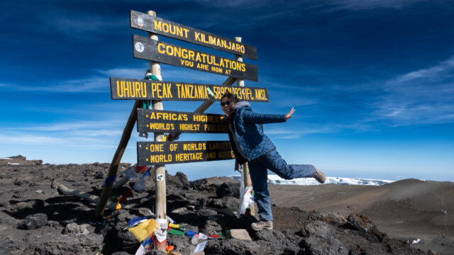 Climber at the Uhuru Peak summit sign on Mount Kilimanjaro in Tanzania.