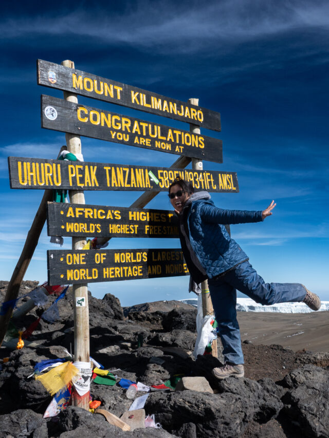 Climber posing at the Uhuru Peak summit sign on Mount Kilimanjaro.
