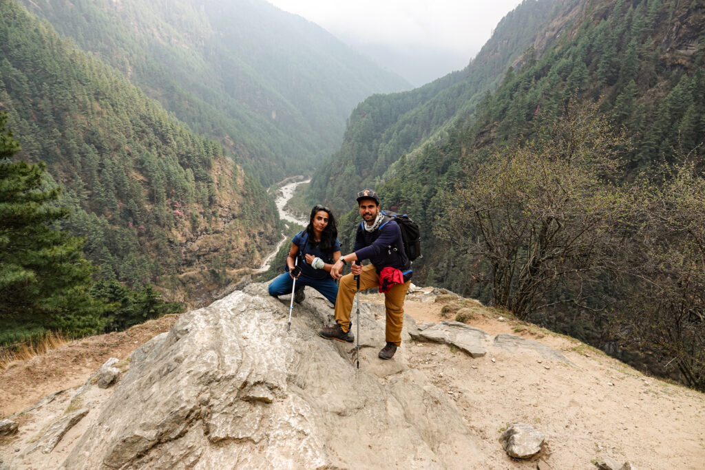 Trekkers resting with hiking poles above a forested valley on the Everest Base Camp trail in Nepal