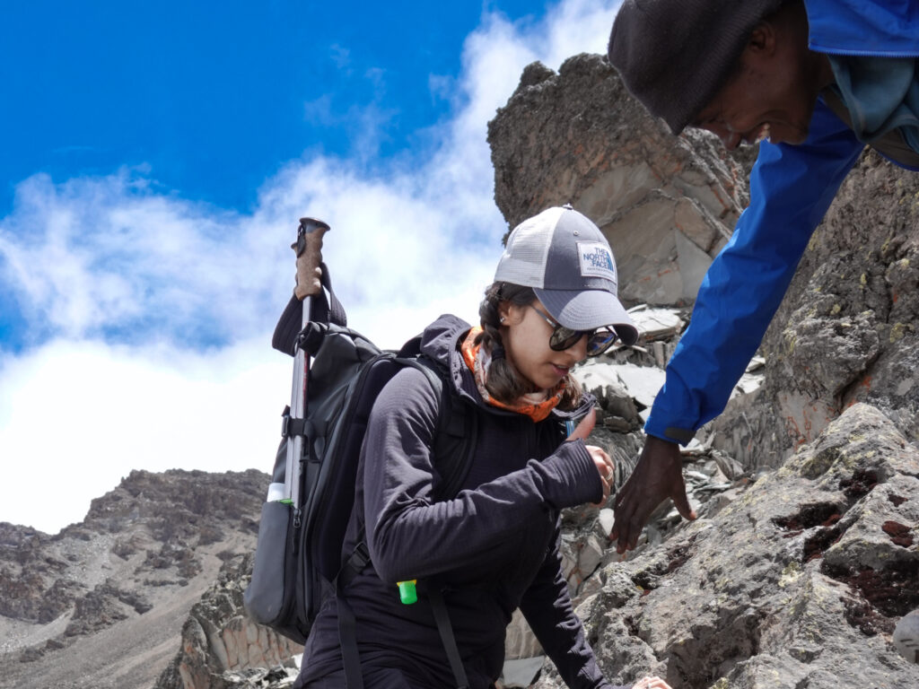 Kilimanjaro guide supporting a hiker on rocky terrain during the climb