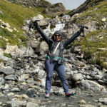 Solo hiker celebrating on a rocky Tour du Mont Blanc trail beside a mountain stream