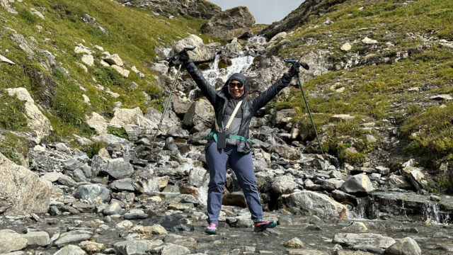 Solo hiker celebrating on a rocky Tour du Mont Blanc trail beside a mountain stream