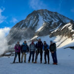 Life Happens Outdoors trekkers standing on snow beneath a steep alpine peak during a high altitude preparation climb.